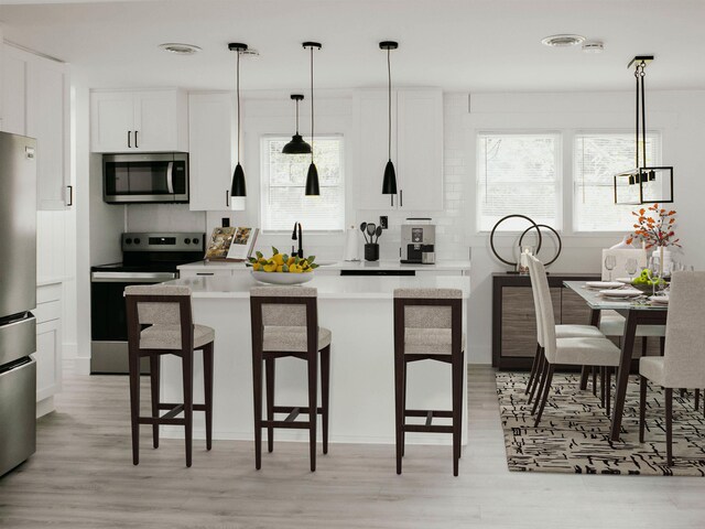 kitchen with pendant lighting, sink, appliances with stainless steel finishes, white cabinetry, and a kitchen bar