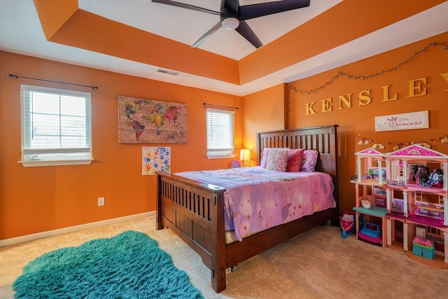 carpeted bedroom featuring multiple windows, ceiling fan, and a raised ceiling