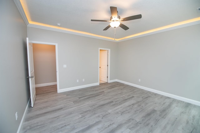spare room with a tray ceiling, a ceiling fan, baseboards, and light wood-style flooring
