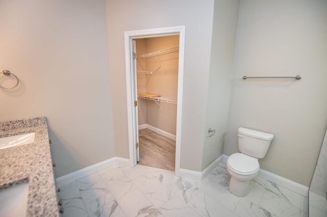full bathroom featuring marble look tiles, toilet, a walk in closet, and baseboards