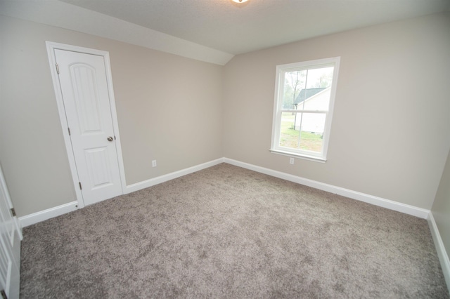 spare room featuring carpet floors, vaulted ceiling, and baseboards