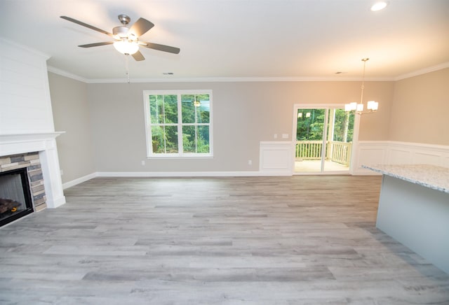 unfurnished living room featuring a chandelier, a stone fireplace, ornamental molding, ceiling fan, and light wood-style floors