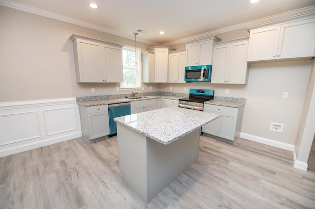 kitchen with appliances with stainless steel finishes, a sink, crown molding, a kitchen island, and light stone countertops