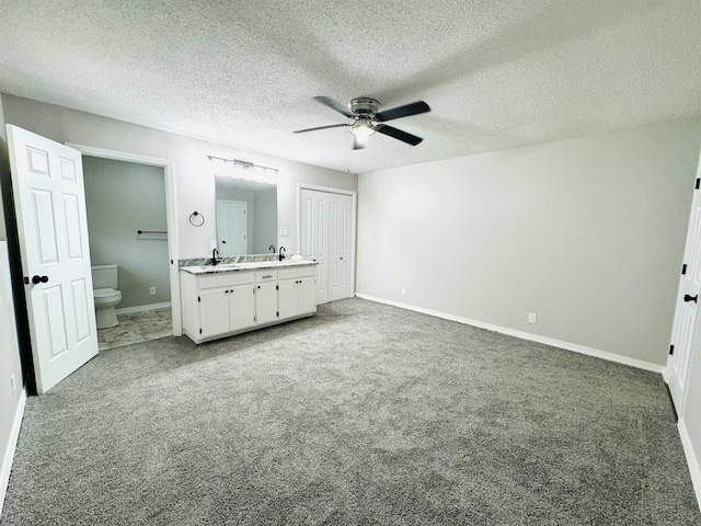 unfurnished bedroom with ceiling fan, carpet floors, a textured ceiling, and ensuite bath