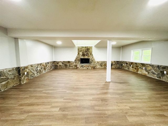 basement featuring a stone fireplace and light wood-type flooring