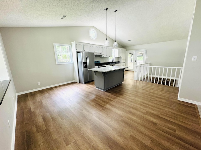 kitchen featuring white cabinetry, hanging light fixtures, stainless steel fridge, vaulted ceiling, and a kitchen island