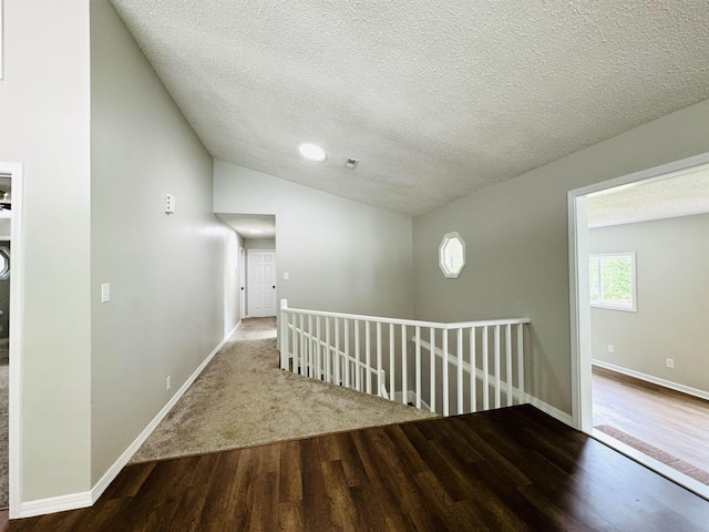 hall featuring hardwood / wood-style floors, lofted ceiling, and a textured ceiling