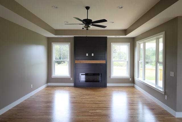 unfurnished living room with a healthy amount of sunlight, a large fireplace, light hardwood / wood-style floors, and a tray ceiling