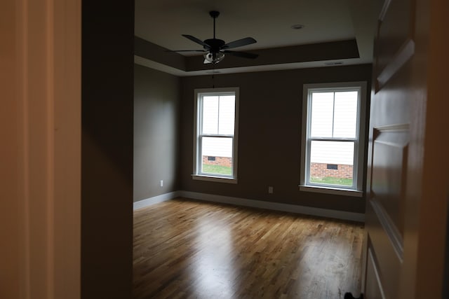 empty room featuring a raised ceiling, hardwood / wood-style flooring, and ceiling fan