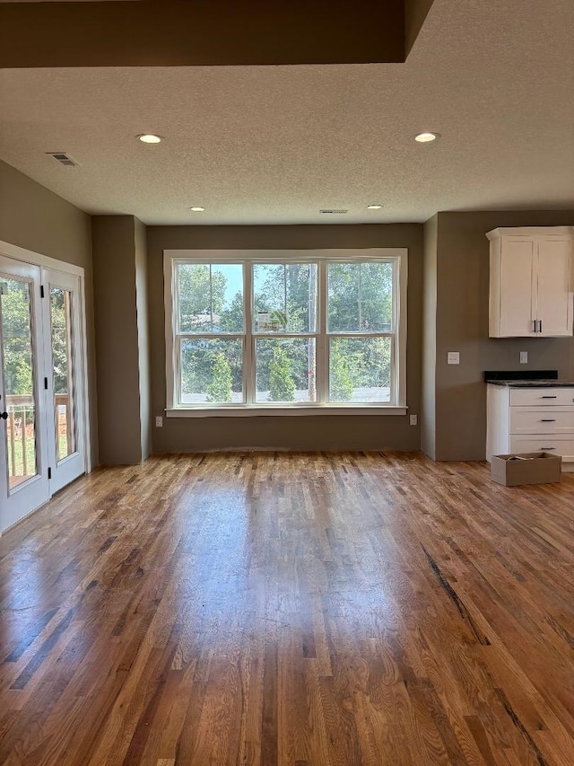 unfurnished living room featuring a healthy amount of sunlight, a textured ceiling, and dark hardwood / wood-style flooring