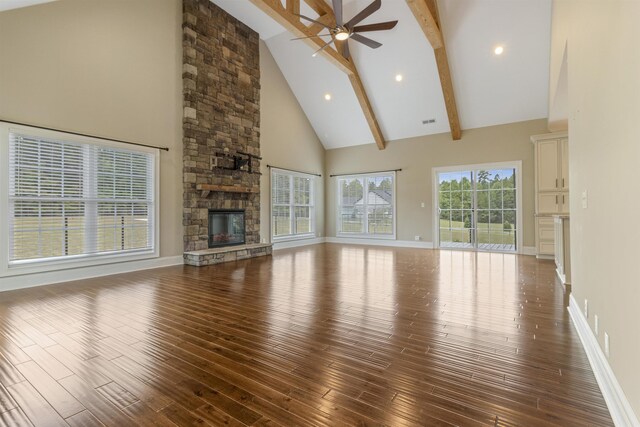 unfurnished living room featuring a stone fireplace, high vaulted ceiling, dark hardwood / wood-style floors, ceiling fan, and beam ceiling