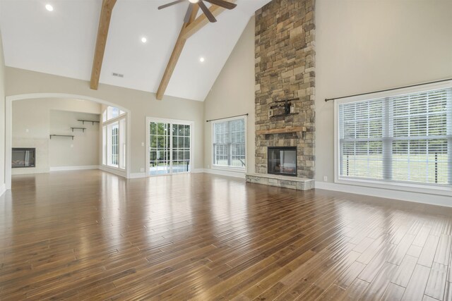 unfurnished living room with a stone fireplace, high vaulted ceiling, ceiling fan, beam ceiling, and hardwood / wood-style floors