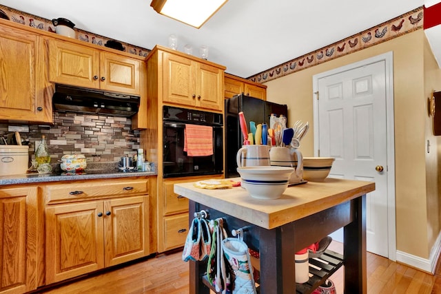 kitchen featuring decorative backsplash, light hardwood / wood-style flooring, extractor fan, and black appliances