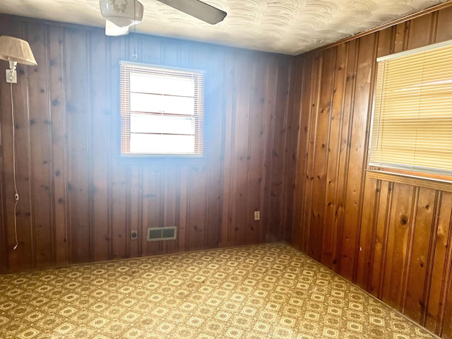 unfurnished room with visible vents, light floors, and wood walls