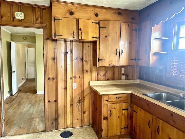 kitchen with brown cabinetry, wood walls, light countertops, and a sink