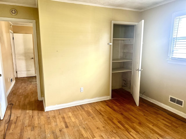 unfurnished bedroom featuring light wood-type flooring, visible vents, baseboards, and ornamental molding