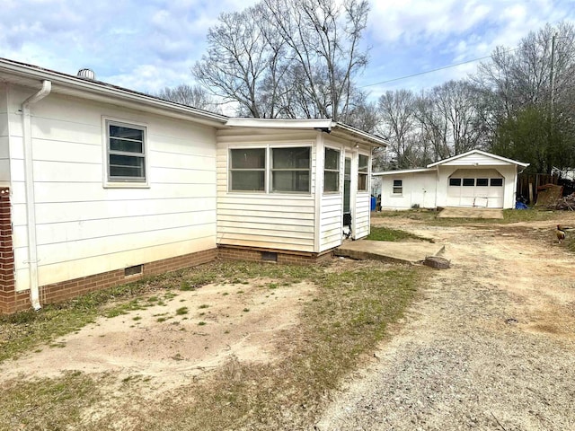 view of property exterior with crawl space, a detached garage, and dirt driveway