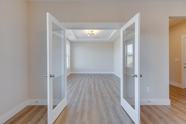 hallway featuring french doors, a tray ceiling, and light hardwood / wood-style floors