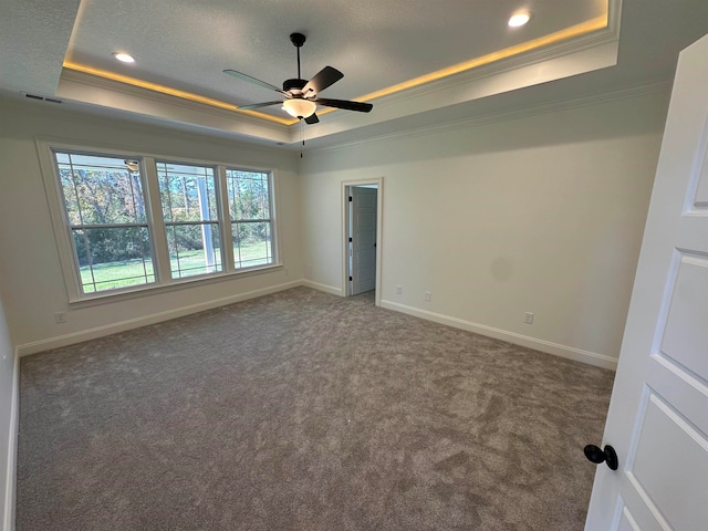 empty room with crown molding, dark colored carpet, a tray ceiling, and ceiling fan