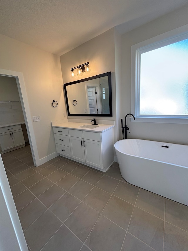 bathroom with a tub to relax in, tile patterned floors, vanity, and a textured ceiling