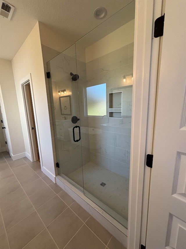 bathroom featuring a shower with shower door, tile patterned flooring, and a textured ceiling