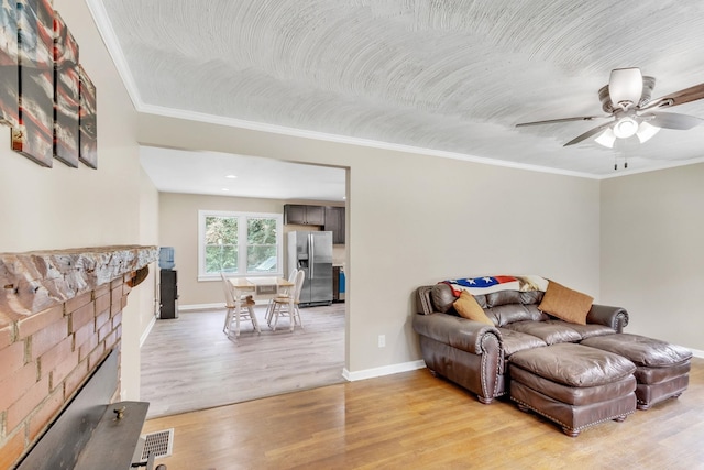 living room featuring crown molding, ceiling fan, a fireplace, and light hardwood / wood-style floors