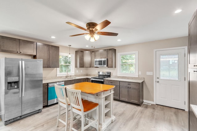 kitchen with stainless steel appliances, sink, pendant lighting, and light wood-type flooring