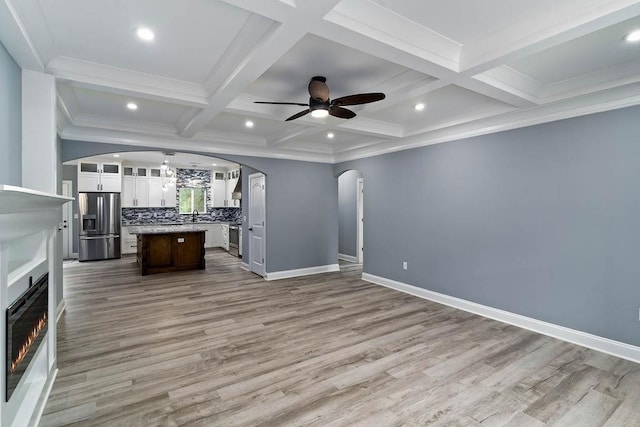 unfurnished living room with baseboards, arched walkways, a ceiling fan, coffered ceiling, and beam ceiling