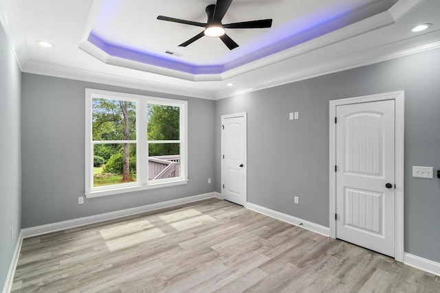 spare room with a tray ceiling, crown molding, ceiling fan, light wood-type flooring, and baseboards