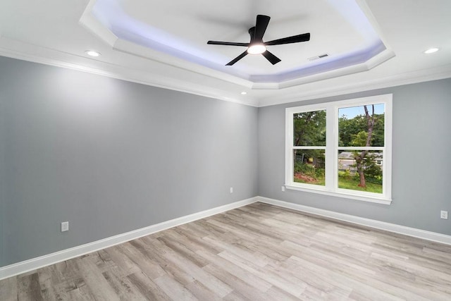 empty room featuring light wood-type flooring, a tray ceiling, visible vents, and baseboards