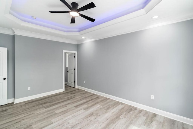 spare room with ceiling fan, baseboards, light wood finished floors, a raised ceiling, and crown molding