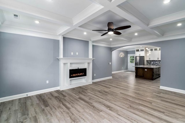 unfurnished living room with a warm lit fireplace, baseboards, beam ceiling, and light wood-style floors