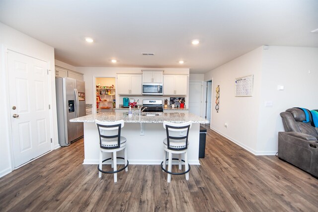 kitchen with light stone counters, appliances with stainless steel finishes, a kitchen breakfast bar, an island with sink, and white cabinets