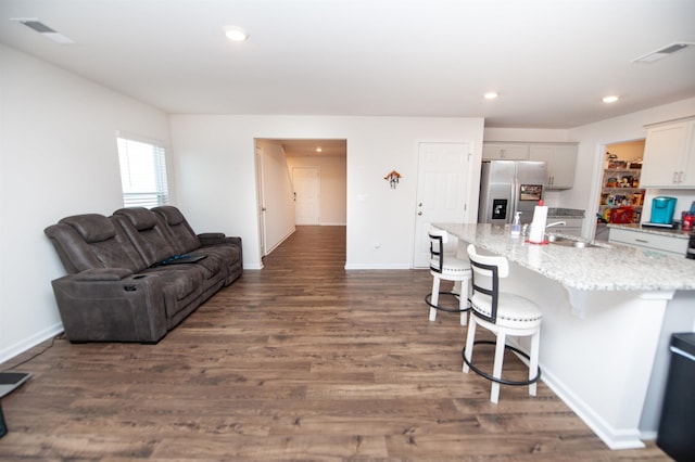 kitchen featuring dark wood-type flooring, a breakfast bar, sink, stainless steel fridge with ice dispenser, and an island with sink