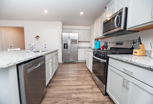 kitchen featuring sink, light stone counters, light hardwood / wood-style flooring, stainless steel appliances, and white cabinets