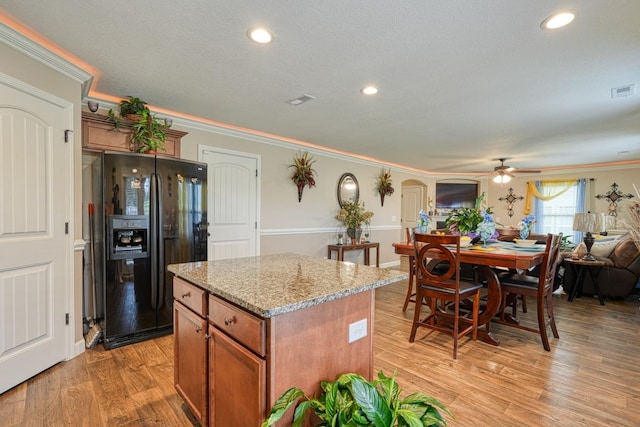 kitchen featuring black fridge, light hardwood / wood-style floors, a center island, ornamental molding, and ceiling fan