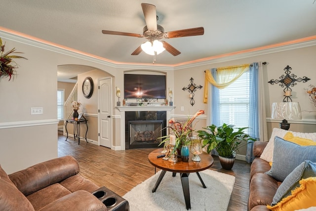 living room with ceiling fan, wood-type flooring, ornamental molding, and a tile fireplace