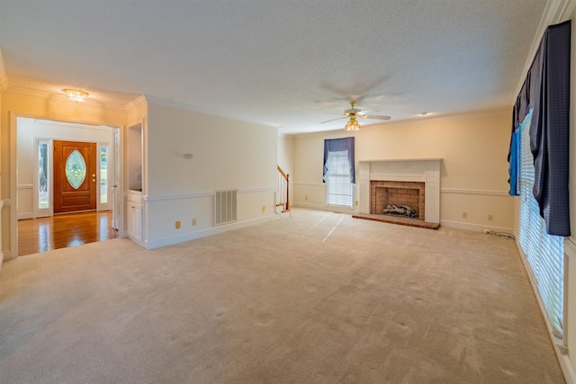 unfurnished living room with a textured ceiling, ceiling fan, crown molding, a fireplace, and light colored carpet