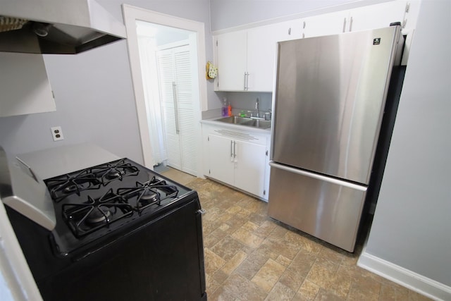 kitchen featuring sink, stainless steel refrigerator, white cabinetry, black range with gas stovetop, and wall chimney exhaust hood