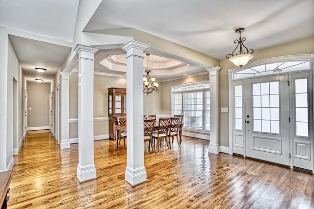 foyer featuring hardwood / wood-style floors, ornamental molding, ornate columns, a raised ceiling, and a chandelier