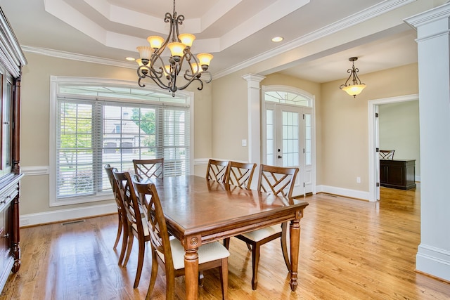 dining space featuring crown molding, decorative columns, a raised ceiling, an inviting chandelier, and light hardwood / wood-style flooring