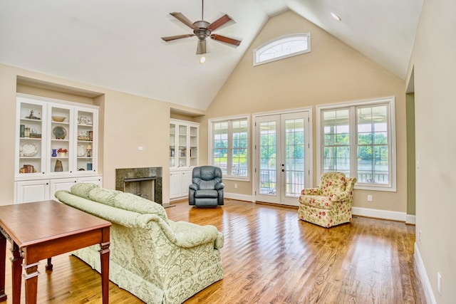 living room with light wood-type flooring, high vaulted ceiling, ceiling fan, french doors, and a premium fireplace