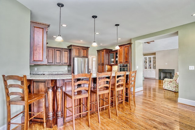 kitchen featuring pendant lighting, light stone countertops, a kitchen breakfast bar, light wood-type flooring, and stainless steel appliances