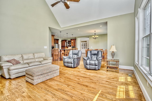 living room featuring ceiling fan with notable chandelier, light wood-type flooring, and high vaulted ceiling