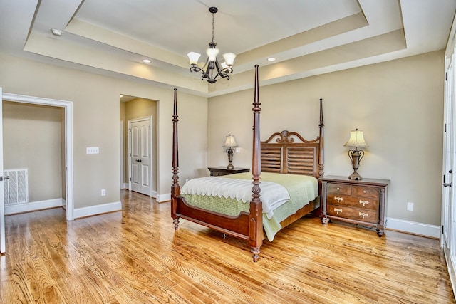 bedroom featuring a notable chandelier, a tray ceiling, and light wood-type flooring