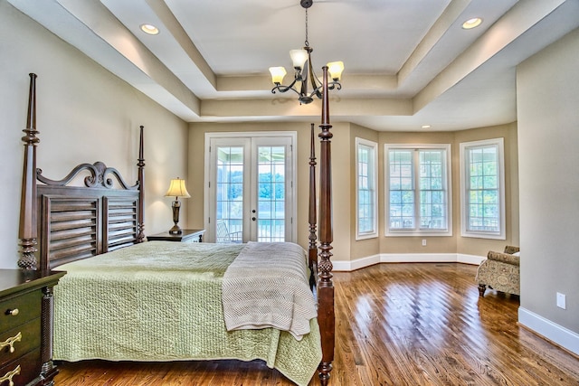 bedroom with a notable chandelier, dark hardwood / wood-style floors, french doors, and a tray ceiling