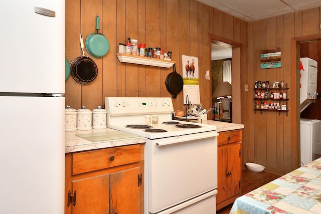 kitchen featuring stacked washer / dryer, wood walls, light countertops, brown cabinetry, and white appliances