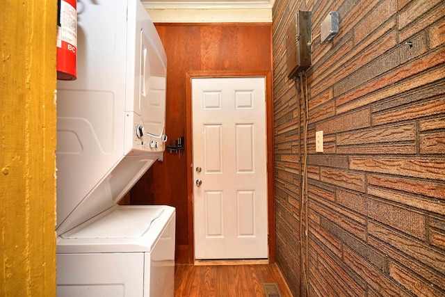 clothes washing area featuring wood finished floors, visible vents, laundry area, wood walls, and stacked washer / dryer