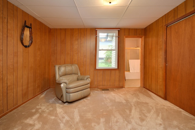 living area featuring a drop ceiling, carpet, visible vents, and wood walls