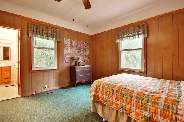 bedroom with carpet floors, wood walls, ceiling fan, and ensuite bath